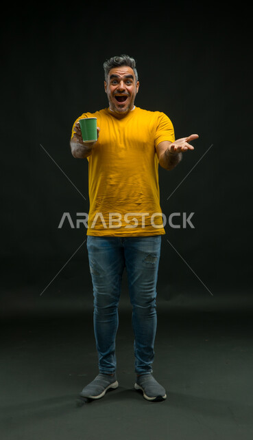 الاندهاش بالمذاق المتميز للمشروبات الساخنة، تعديل المزاج بتناول الكافيين، بورتريه لرجل عربي خليجي سعودي يرتدي الزي كاجوال يشير بيده إلى كوب من الورق المقوى, صورة لكامل الجسم، النظر إلى الكاميرا بإيماءات الذهول والتعجب، خلفية سوداء .