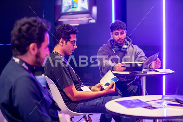 التوعية ضد الاختراق الغير قانوني, مجموعه من الشباب العرب الخليجيين السعودينن يجلسون على الطاولة ويقومون بالاطلاع على القواعد التعليمية حول منظمة بلاك هات للامن السيبراني، استكشاف الابتكارات في مجال السايبر سكيوريتي, فعاليات موسم الرياض