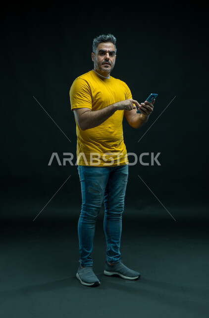الشعور بالانزعاج لعدم توفر الانترنت، إستخدام التطبيقات عبر الهاتف الذكي، مشاهدة الأخبار المفاجئة السيئة عبر الجوال، بورتريه لشاب عربي خليجي سعودي يرتدي الزي الكاجوال ينظر إلى الكاميرا بتعابير الجدية، صورة الجسم بالطول الكامل، خلفيه سوداء