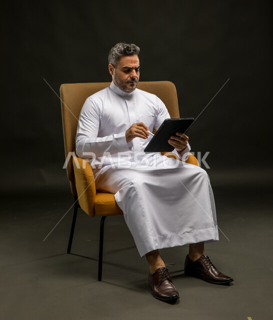 قراءة الأخبار السيئة والمزعجة، تصفح تطبيقات الهاتف المحمول، التواصل مع الأهل والاصدقاء عبر الانترنت، بورتريه لشاب عربي خليجي سعودي  يرتدي الزي التقليدي يقوم بمتابعة مواقع ووسائل التواصل الاجتماعي عبر الجوال بإيماءات العبوس، خلفية سوداء