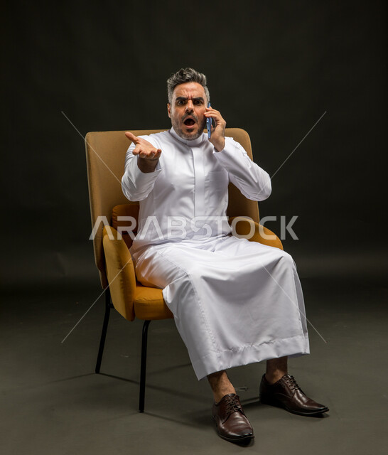 الخسارة في الصفقات المالية، استخدام أجهزة التواصل الحديثة والمتطورة, الشعور بالانزعاج لسماع الأخبار السيئة, بورتريه لرجل عربي خليجي سعودي يرتدي الزي التقليدي يقوم بإجراء مكالمة هاتفية عبر الهاتف المحمول بإيماءات الصدمة والعبوس والغضب, خلفية سوداء