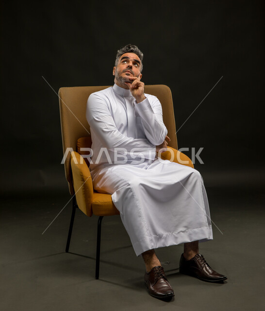 التأمل وشرود الذهن والتخطيط للمستقبل، التفكير لأيجاد حل مشكلة ما، مواجهة المشكلات والتحديات في الحياة العملية، بورتريه لرجل عربي خليجي سعودي يرتدي الثوب التقليدي يجلس على الكرسي وينظر الى الأعلى بإيماءات التمعن والتركيز، خلفية سوداء