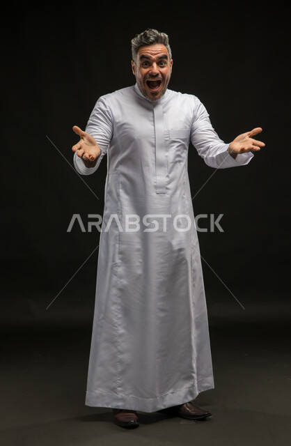 تعابير وايماءات الاندهاش والسرور برؤية شخص ما، الترحيب والاستقبال بحرارة وحب، بورتريه لرجل عربي سعودي خليجي يرتدي الثوب التقليدي يفتح كفيه ينظر الى الكاميرا, صورة الجسم بالطول الكامل, خلفية سوداء .