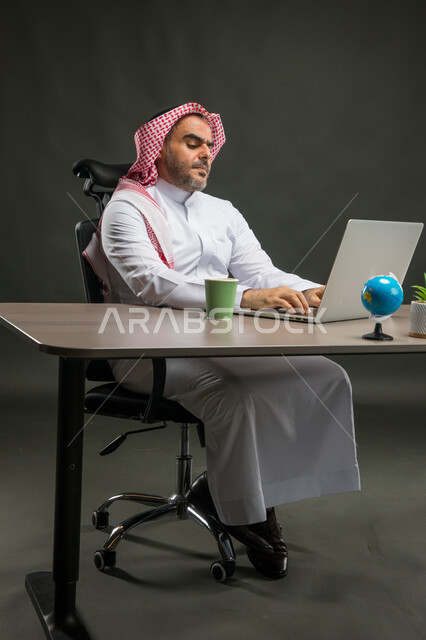 إيماءات الانزعاج والضغط العصبي، الشعور بالتعب خلال فترة العمل، بورتريه لرجل اعمال عربي خليجي سعودي يرتدي الشماغ والثوب التقليدي يجلس في مكتبه يستخدم الحاسوب المحمول، إنجاز مهام العمل اليومية، خلفية سوداء