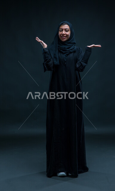 ممارسة الالعاب الحركية ،قضاء اوقات ممتعه بالتسلية والترفيه , بورتريه لامرأة عربيه خليجية سعوديه ترفع يديها للاعلى بإشارات تدل على المفاجأة و اللعب ,خلفية سوداء