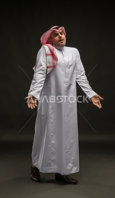 الشعور بالحيرة وعدم المعرفة، بورتريه لرجل عربي سعودي خليجيي يرتدي الشماغ والثوب التقليدي يرفع يفتح كفيه بإيماءات عدم التأكد, التردد وعدم الثقة بخصوص أمر معين، الوقوف باستقامة والنظر إلى الكاميرا، صورة الجسم بالطول الكامل,خلفية سوداء .