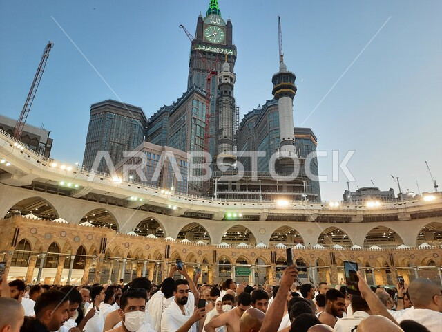 The clock tower overlooking the Grand Mosque in Mecca at sunset, luxury hotels and towers surrounding the mosque, Islamic gathering from all over the world to perform worship and get closer to God, sacred Islamic religious places and landmarks, pilgrims and Umrah pilgrims in the Holy House of God