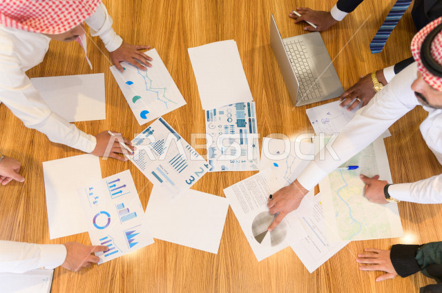 اجتماع اداري مع مجموعة من الأشخاص السعوديين الخليجيين في غرفة الاجتماعات  ، اجتماع رجال اعمال و سيده اعمال سويا داخل الشركة ، مجموعة من الاوراق المبعثرة على طاولة الاجتماعات ،  شركة سعودية ، عمل خليجي ،  فريق العمل 