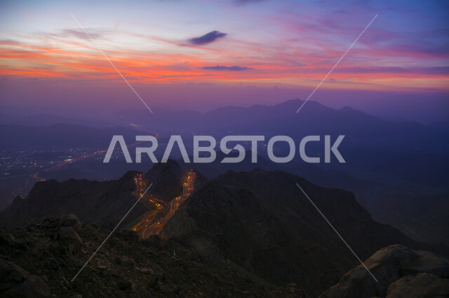 البيئة الجبلية والقمم والمرتفعات في المملكة العربية السعودية، صورة جوية من الأعلى لحركة مرور وسير السيارات على جبال الهدا في مدينة الطائف، منظر غروب الشمس فوق طريق اسفلتي ملتوي وعر وسط الجبال الصخرية في منطقة عقبة الهدا