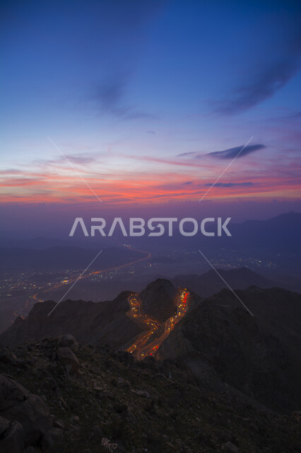 طريق اسفلتي ملتوي وعر وسط الجبال الصخرية في منطقة عقبة الهدا, البيئة الجبلية والقمم والمرتفعات في المملكة العربية السعودية، صورة جوية من الأعلى لحركة مرور وسير السيارات على جبال الهدا في مدينة الطائف وقت غروب الشمس