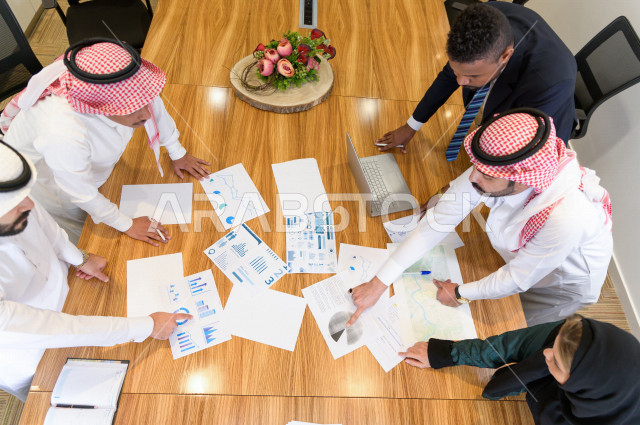اجتماع اداري مع مجموعة من الأشخاص السعوديين الخليجيين في غرفة الاجتماعات  ، اجتماع رجال اعمال و سيده اعمال سويا داخل الشركة ، مجموعة من الاوراق المبعثرة على طاولة الاجتماعات ،  شركة سعودية ، عمل خليجي ،  فريق العمل 