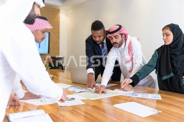 اجتماع اداري مع مجموعة من الأشخاص السعوديين الخليجيين في غرفة الاجتماعات  ، اجتماع رجال اعمال و سيده اعمال سويا داخل الشركة ، مجموعة من الاوراق المبعثرة على طاولة الاجتماعات ،  شركة سعودية ، عمل خليجي ،  فريق العمل 