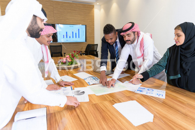 اجتماع اداري مع مجموعة من الأشخاص السعوديين الخليجيين في غرفة الاجتماعات  ، اجتماع رجال اعمال و سيده اعمال سويا داخل الشركة ، مجموعة من الاوراق المبعثرة على طاولة الاجتماعات ،  شركة سعودية ، عمل خليجي ،  فريق العمل 