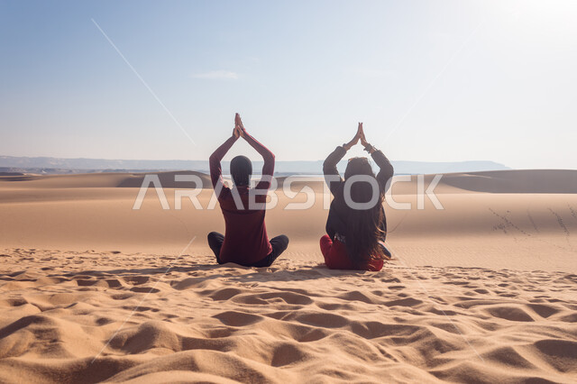 ممارسة الرياضة والهوايات المفضلة, الجلوس والاستمتاع في إحدى مناطق المملكة العربية السعودية, صورة من الخلف لصديقتين عربيتين خليجين سعوديتين يجلسان على الرمال الذهبية الناعمة, التسلية والترفيه وقضاء وقت ممتع مع الأصدقاء, رحلات السفاري الترفيهية