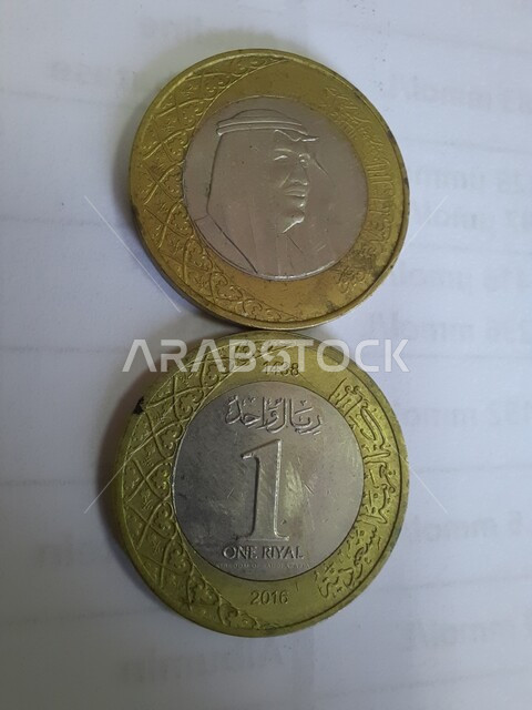 نقش خادم الحرمين الشريفين الملك عبد الله بن عبد العزيز آل سعود، العملة الرسمية للمملكة العربية السعودية، التمويل والاستثمار المالي، صورة مقربة لاثنتان من القطع المعدنية التاريخية القديمة من فئة ١ واحد ريال، نقود وعملات حديدية متداولة، خلفية بيضاء .