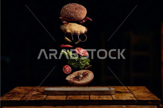 صورة لمكونات ساندوتش البرجر المتطايرة، وجبة الهمبرجر اللذيذة بقطع اللحم المشوي وشرائح الجبن الذائبة والخضراوات الطازجة على طبق خشبي, وصفات الطعام الغير صحية، مطاعم للمأكولات السريعة في المملكة العربية السعودية, خلفية سوداء .