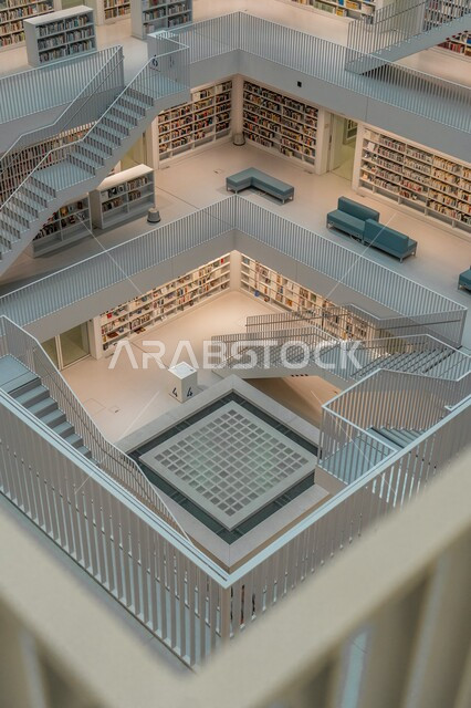 الفن الهندسي المعماري في الديكورات الداخلية، موسوعة غنية بمختلف أنواع الكتب والروايات، صورة من الأعلى لمكتبة بتصاميم عصرية فاخرة، أثاث مكتبي متميز ، بناء متعدد الطوابق بسلالم وأدراج، جدران وارضيات رخامية بيضاء .