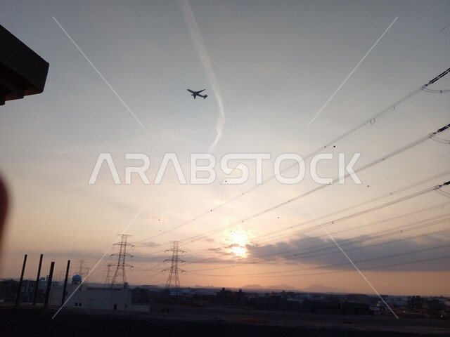 High-voltage electrical transmission towers, electricity distribution poles and lines in cities, a plane flying in the sky of the Kingdom of Saudi Arabia, interest and progress in infrastructure work, supplying and serving areas with electrical energy.