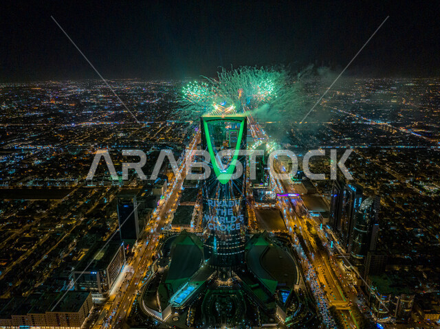 التطور و النمو الاقتصادي, قذف الألعاب النارية امام برج المملكة المضيئ باللون الاخضر في وقت الليل أثناء الاحتفال في مناسبة الفوز في معرض اكسبو 2030 في السعودية، عروض ثقافية و أنشطه ترفيهية، صورة من الاعلى للفن الهندسي المعماري على الطراز الحديث