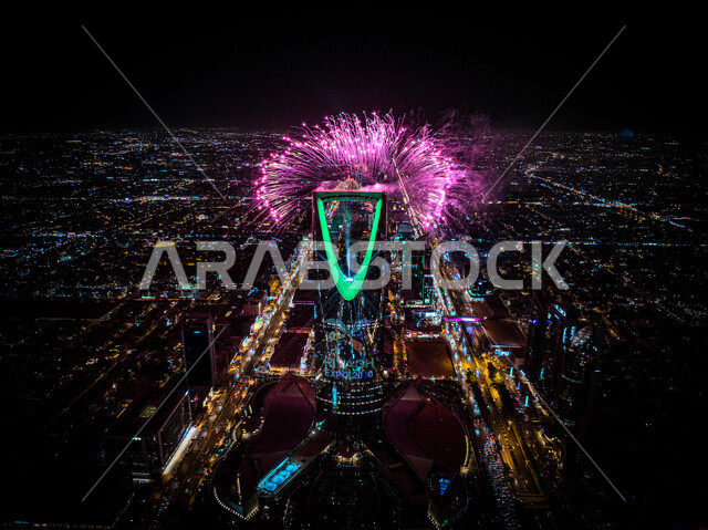 قذف الألعاب النارية باللون البنفسجي امام برج المملكة المضيئ باللون الاخضر في وقت الليل أثناء الاحتفال في مناسبة الفوز في معرض اكسبو 2030 في السعودية، التطور و النمو الاقتصادي, عروض ثقافية و أنشطه ترفيهية، صورة من الاعلى للفن الهندسي المعماري على الطراز الحديث