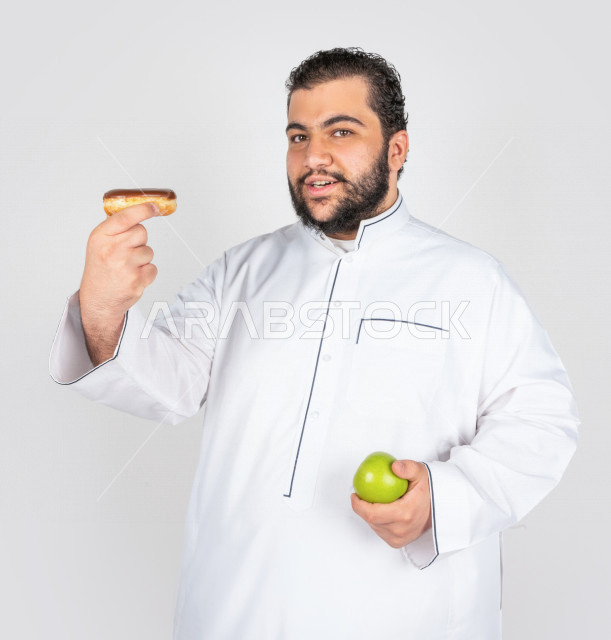 بورتريه شاب سعودي خليجي سمين في خيرة بين السكريات و الأكل الصحي ، يعاني من السمنة ، مشاكل صحية ،الوزن الزائد والسمنة ، خسارة السعرات الحرارية  ، اتباع نظام صحي