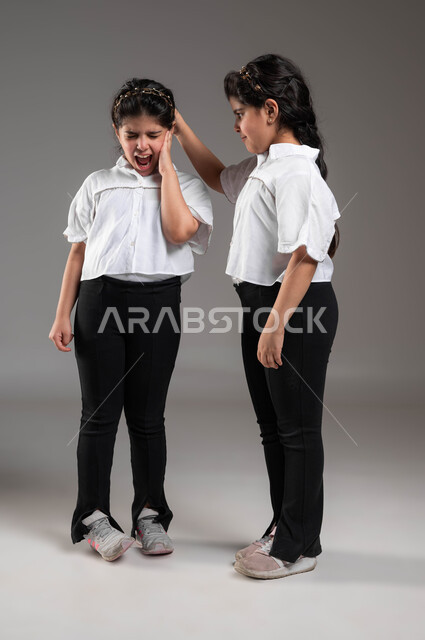 سوء التفاهم والنقاش الحاد بين الأخوة، الغضب والقاء اللوم، التوترات والضغوط العائلية، بورتريه لأختين توأم عربيتين خليجيتين سعوديتين تتشاجران مع بعضهما، ازمة في العلاقات الاسرية، صورة لكامل الجسم، خلفية رمادية