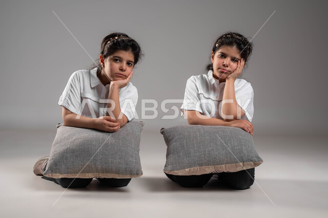 الشعور والاحساس بالضجر والزهق، بورتريه لأختين توأم عربيتين خليجيتين سعوديتين تجلسان بملل وايماءات العبوس والانزعاج، انتظار شيء ما، التفكير وشرود الذهن، خلفية رمادية