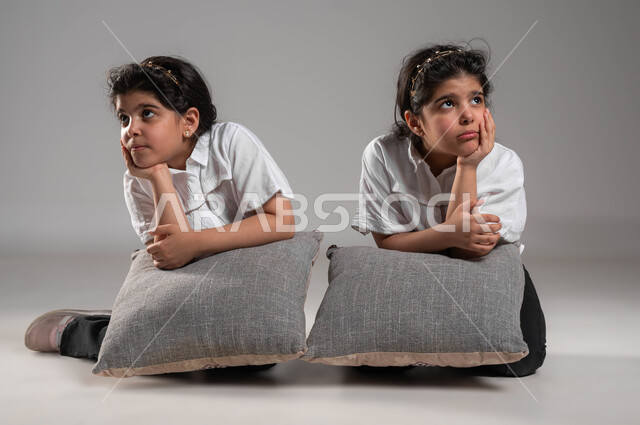 الاحساس والشعور بالضجر والزهق، انتظار شيء ما، بورتريه لأختين توأم عربيتين خليجيتين سعوديتين تجلسان بملل وايماءات العبوس والانزعاج، شرود الذهن والتفكير، خلفية رمادية