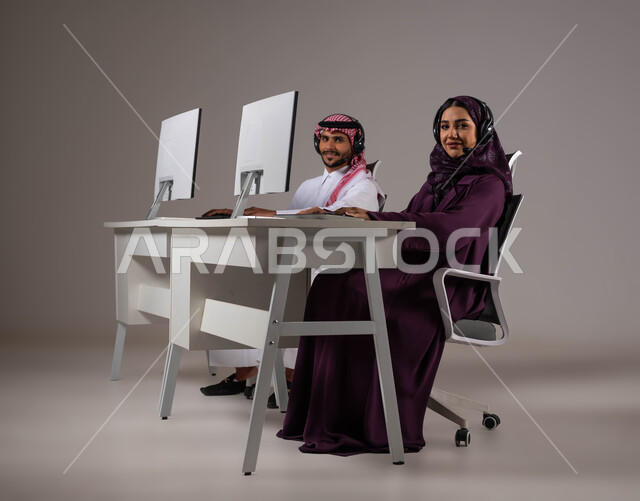 زيادة مستوى رضا العميل، مفهوم المشاركة و التعاون في العمل ،الإجابة على الاستعلامات والاستفسارات, بورتريه لرجل و امرأة عربيان سعوديان خليجيان يعملان في خدمة العملاء ينظران إلى الكاميرا يرتديان سماعة الاتصال, مهن ووظائف سعودية، خلفية رمادية