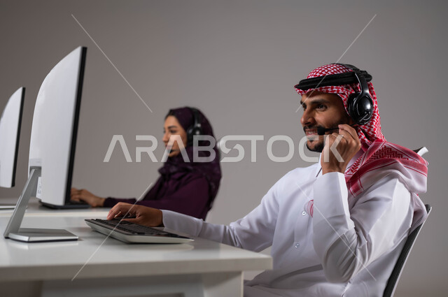 وظائف ومهن سعودية، تقديم الخدمات المطلوبة والحرص على رضى العميل، الإجابة على الاستفسارات و الاستعلامات ،ارتداء سماعة الاتصال للتواصل مع العملاء ،بورتريه مقرب لموظفان عربيان سعوديان خليجيان يعملان في خدمة العملاء ويجلسون في مقر العمل ،خلفية رمادية