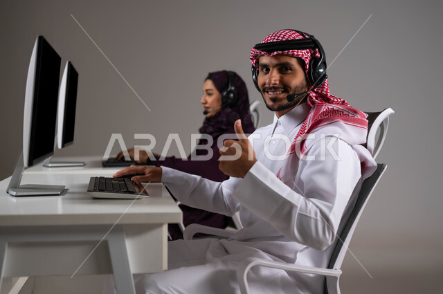 الإجابة على الاستفسارات و الاستعلامات, النظر إلى الكاميرا بايماءات السرور ورفع اليد بعلامة الجودة ،تطوير و متابعه العمل في الشركات السعودية، ارتداء سماعة الاتصال للتواصل مع العملاء ،بورتريه لموظفان عربيان سعوديان خليجيان يعملان في خدمة العملاء ،خلفية رمادية