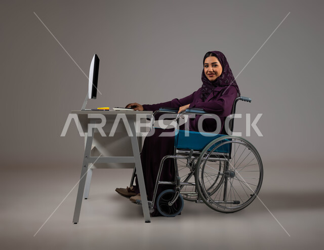 دمج و توظيف ذوي الاعاقه في مختلف المجالات, بورتريه لموظفة عربية سعودية خليجية محجبة مبتسمة من ذوي الهمم تنظر إلى الكاميرا تجلس في مقر العمل, اهتمام  ودعم المجتمع السعودي لذوي الاحتياجات الخاصه, الشعور بالراحه والطمأنينه، خلفية رمادية .