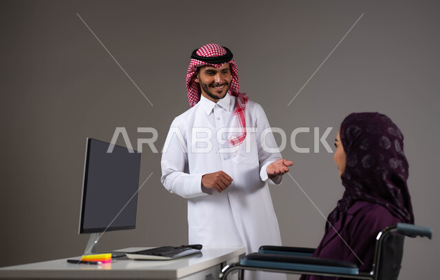 تمكين اصحاب الهمم وذوي الاحتياجات الخاصة من الدخول الى مجال العمل، بورتريه مقرب لزميلين عربيين خليجيين سعوديين يقومان بإنجاز المهام عبر الحاسوب المحمول داخل المكتب، دمج العمل مع التقنية والتكنولوجيا، تبادل الافكار والخبرات لتحقيق اهداف الشركة، خلفية رمادية