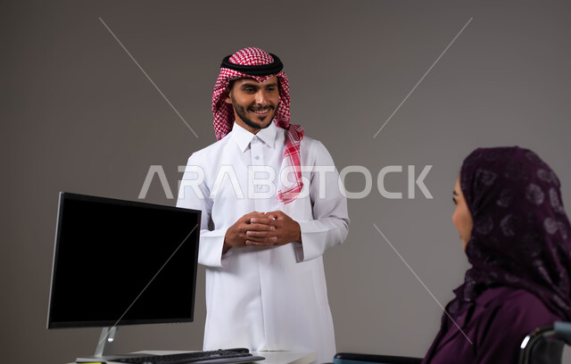 الإنصات الى الملاحظات بحب وشغف، تمكين اصحاب الهمم وذوي الاحتياجات الخاصة من الدخول الى مجال العمل، بورتريه مقرب لزميلين عربيين خليجيين سعوديين مبتسمين يقومان بإنجاز المهام عبر الحاسوب المحمول داخل المكتب، دمج العمل مع التقنية والتكنولوجيا، خلفية رمادية