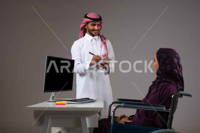 تدوين الملاحظات لتطوير خطط الشركة، دمج العمل مع التقنية والتكنولوجيا، اتاحة الفرصة امام ذوي الهمم بالدخول الى مجال العمل، بورتريه مقرب لزميلين عربيين خليجيين سعوديين مبتسمين يقومان بإنجاز المهام عبر الحاسوب المحمول داخل المكتب، روح الفريق الواحد، خلفيه رمادية