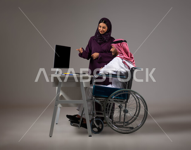 توفير بيئة عمل مناسبة للمعوقين، الاشارة الى اللابتوب والتنبيه لتطبيق الخطط، تبادل الأفكار والخبرات لتحقيق الأهداف، بورتريه لزميلين عربيين خليجيين سعوديين مبتسمين يقومان بإنجاز المهام عبر الحاسوب المحمول داخل المكتب، دمج ذوي الهمم بالحياة العملية، خلفيه رمادية