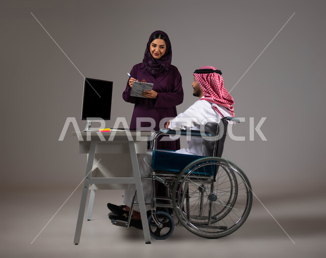 روح الفريق الواحد، دمج العمل مع التقنية والتكنولوجيا، اتاحة الفرصة امام ذوي الهمم بالدخول الى مجال العمل، بورتريه لزميلين عربيين خليجيين سعوديين مبتسمين يقومان بإنجاز المهام عبر الحاسوب المحمول داخل المكتب، تدوين الملاحظات لتطوير خطط الشركة، خلفيه رمادية