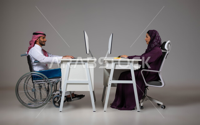 اهتمام ودعم المجتمع السعودي لذوي الاحتياجات الخاصه, بورتريه لموظفان عربيان خليجيان سعوديان يعملان على الحاسوب في مقر الشركة، مفهوم التمكين الاجتماعي, توظيف ودمج المرضى والمعاقين في مختلف المجالات, شعور ذوي الهمم بالراحه والطمأنينه في بيئة العمل، خلفية رمادية