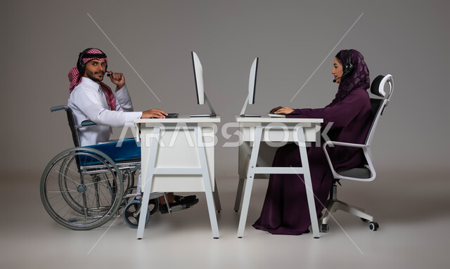 مفهوم التمكين الاجتماعي, توظيف ودمج المرضى والمعاقين في مختلف المجالات,  دعم المجتمع السعودي لذوي الاحتياجات الخاصه, بورتريه لموظفان عربيان خليجيان سعوديان يضعان الهيدفون يعملان في قسم خدمة العملاء، شعور ذوي الهمم بالراحه والطمأنينه في بيئة العمل، خلفية رمادية