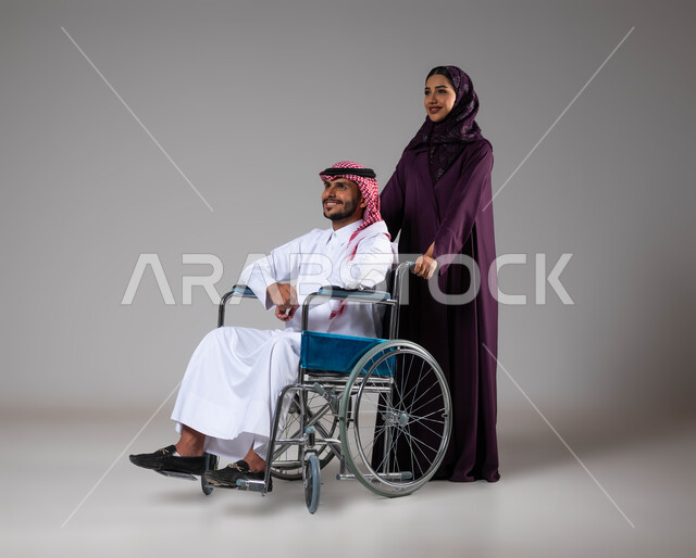 العنايه والاهتمام بأصحاب الهمم، الإخلاص والحنان بين الأزواج, شعور المعاقين بالإنتماء والتقدير في السعوديه، بورتريه لزوجة عربية خليجية سعودية محجبة ترتدي العباءة تقوم بمساعدة زوجها من ذوي الاحتياجات الخاصه، تأمين اجهزة ومعدات تساعد بالحركة والتنقل، خلفية رمادية
