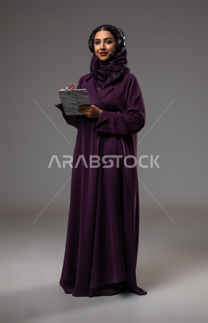تدوين وتسجيل الملاحظات والشكاوي، متابعة وتطوير العمل، مفهوم خدمة العملاء، بورتريه لموظفة عربية خليجية سعودية محجبة مبتسمة ترتدي العباءة تضع سماعات الهيدفون على رأسها تقوم بالكتابة على الاوراق، الرد على الاستفسارت والتساؤلات، صورة الجسم بالكامل، خلفية رمادية