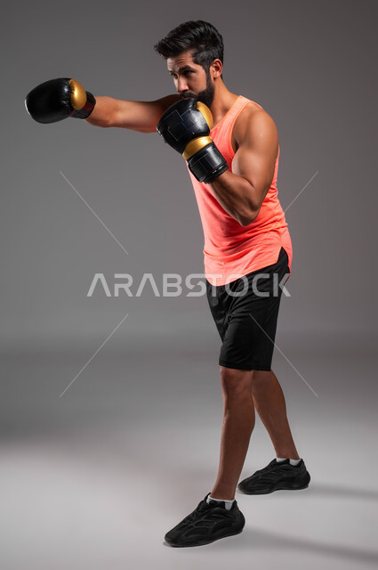 Practicing self-defense, physical activity to maintain health and physical fitness, portrait of a Saudi Arabian Gulf boxer wearing boxing gloves practicing combat movements, wrestling and boxing, full-length body image, gray background