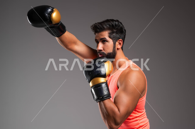 Attack and fighting movements, physical activities to maintain health and physical fitness, a side portrait of a Saudi Gulf Arab boxer wearing sports clothes and boxing gloves practicing boxing, practicing wrestling arts, gray background