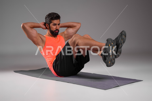 Tightening the abdominal muscles with aerobic training, a portrait of a Saudi Gulf Arab athlete wearing sports clothing doing exercises to maintain physical fitness, the concept of health and fitness, youth activities and sports, gray background