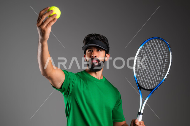 إيماءات تدل على الحماس والاندماج بالتمرين، رياضات شبابية وأنشطة ترفيهية، التدرب على إتقان لعبة البادل، إجراء تمرينات رياضة المضرب، بورتريه مقرب للاعب بادل عربي خليجي سعودي يرتدي ملابس رياضية و يلعب بالكرة والمضرب ، خلفية رمادية