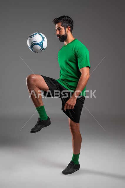 Playing skills and arts, professionalism in dealing with football, a portrait of a Saudi Arabian Gulf player wearing sports clothing playing with the ball, movements of enthusiasm and preparation for the start of the match, full-length body image, gray background
