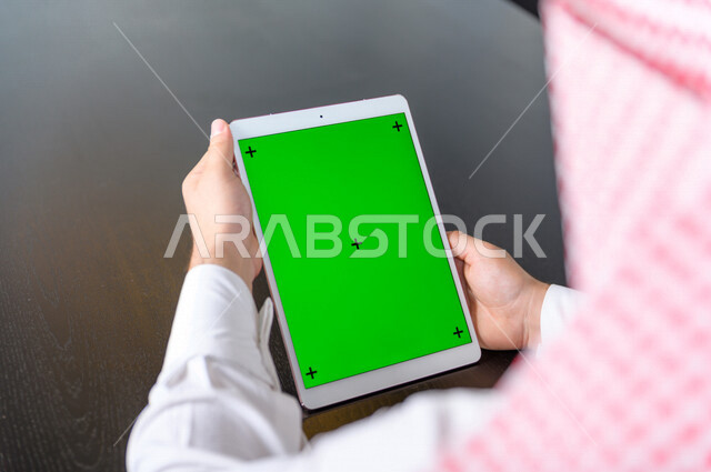 رجل أعمال سعودي خليجي يستخدام جهاز لوحي تابلت بشاشة خضراء كروما ، تقنية و حاسب ، شراء عن بعد ، التعليم عن بعد ، العاب فيديو
