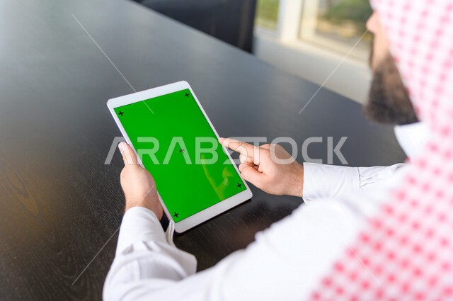رجل أعمال سعودي خليجي يستخدام جهاز لوحي تابلت بشاشة خضراء كروما ، تقنية و حاسب ، شراء عن بعد ، التعليم عن بعد ، العاب فيديو