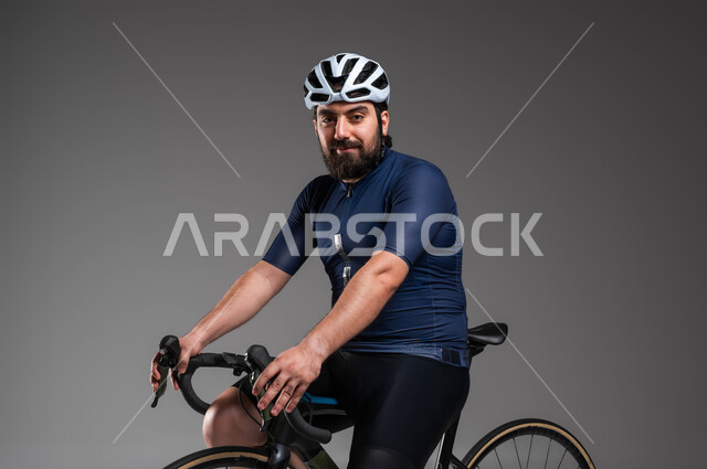 ممارسة الأنشطة البدنية الممتعة، فعاليات ركوب الدراجات في المملكة، مواصلات آمنة في السعودية، بورتريه لرجل عربي خليحي سعودي يرتدي الملابس الرياضية وخوذة الحماية يقوم بقيادة دراجة السباق الهوائية، المحافظة على اللياقة الجسدية، خلفية رمادية