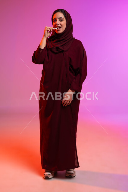 التأكد من نظافة الأسنان بعد تناول الطعام، الاهتمام بالأناقة والمظهر الخارجي، المحافظة على ابتسامة بيضاء، بورتريه لامرأة عربية خليجية سعودية تقوم بتنظيف أسنانها باستخدام الخيط السني، مفهوم العناية بصحة الفم، صورة الجسم بالكامل، خلفية ملونة